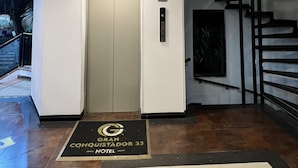 Ein Innenbereich mit einem Flur, einem Aufzug, einer Treppe und einer Fußmatte mit dem Logo des Gran Conquistador 33 Hotels.