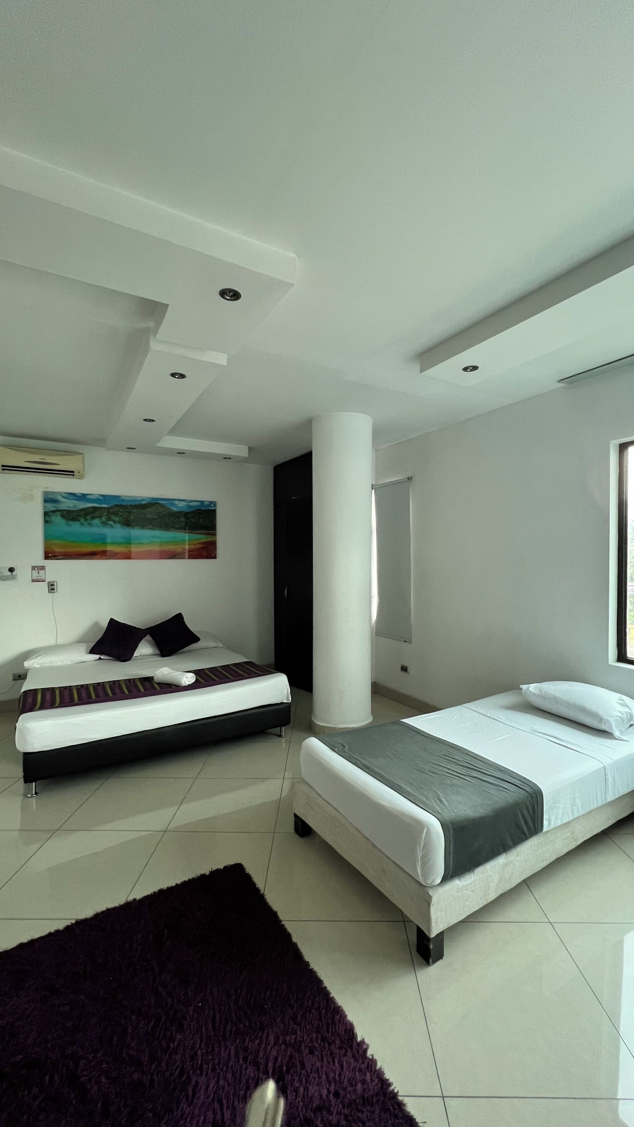A modern hotel room with two beds, a large window, and a painting on the wall.