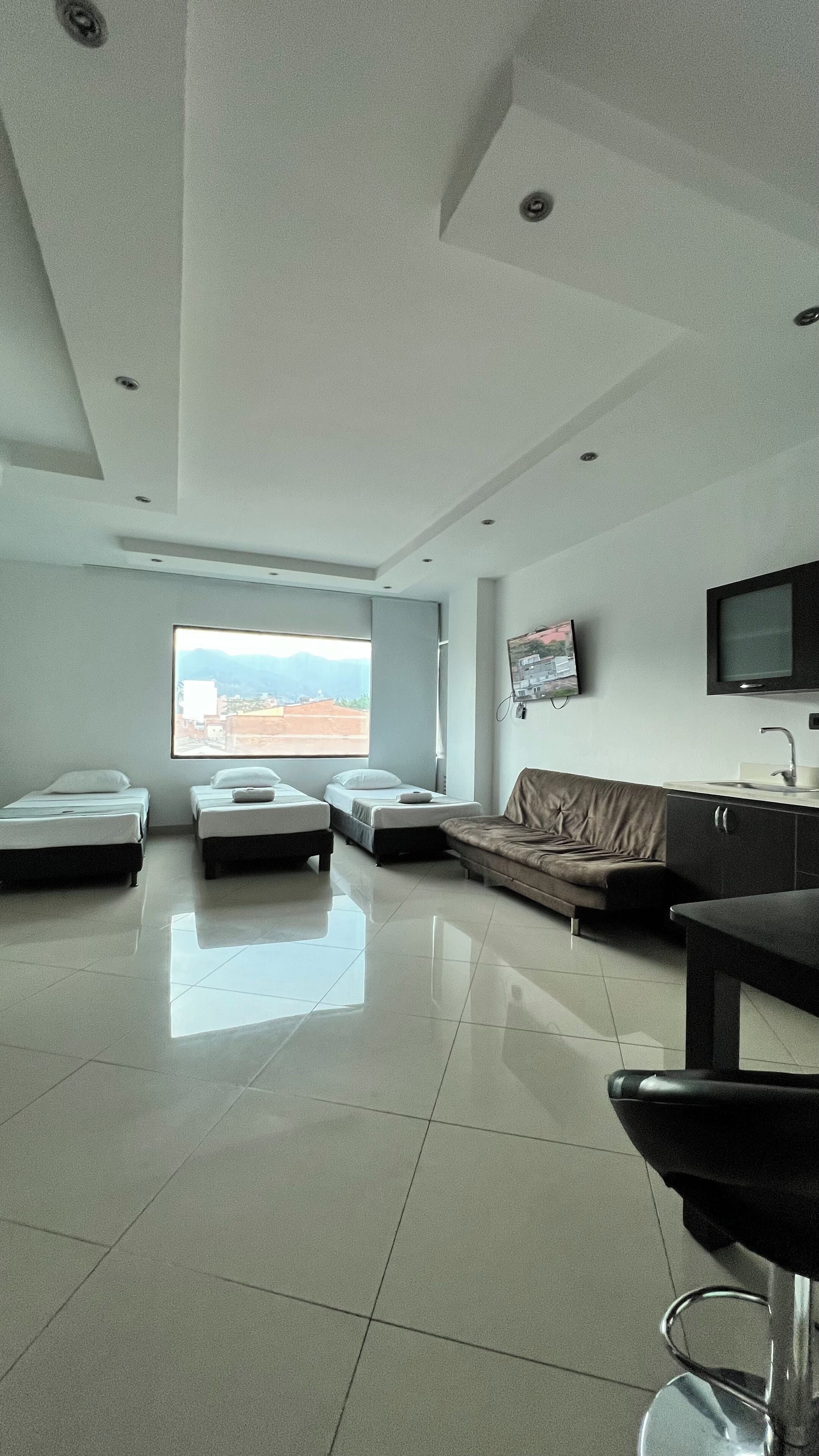 A modern hotel room with two single beds, a sofa, a TV, and a sink.