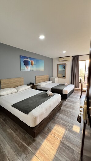 Une chambre d’hôtel avec deux lits, un petit bureau, une chaise et une grande fenêtre avec des rideaux.