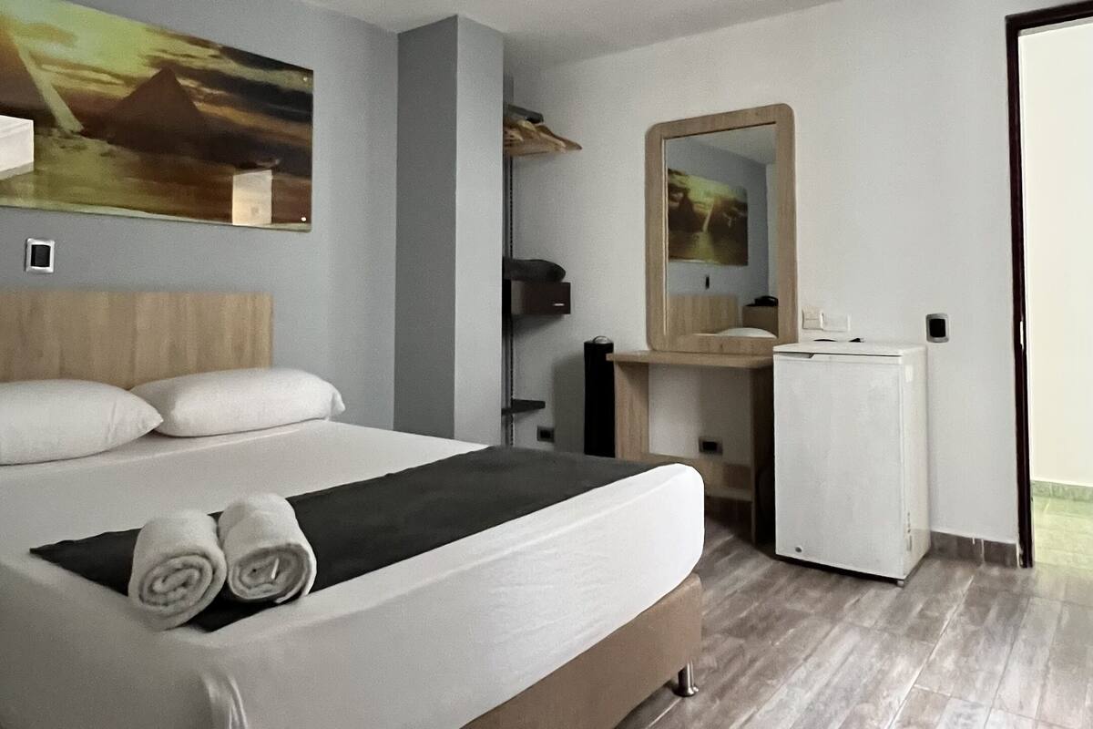 Een moderne hotelkamer met een groot bed, een klein bureau, een spiegel en een schilderij aan de muur.