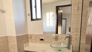 A modern bathroom with a glass sink, a toilet, and a shower area.