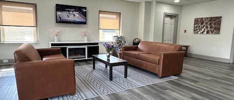 Ein geräumiger Raum mit einem braunen Ledersofa, einem Couchtisch und einem flachbildfernseher an der Wand.