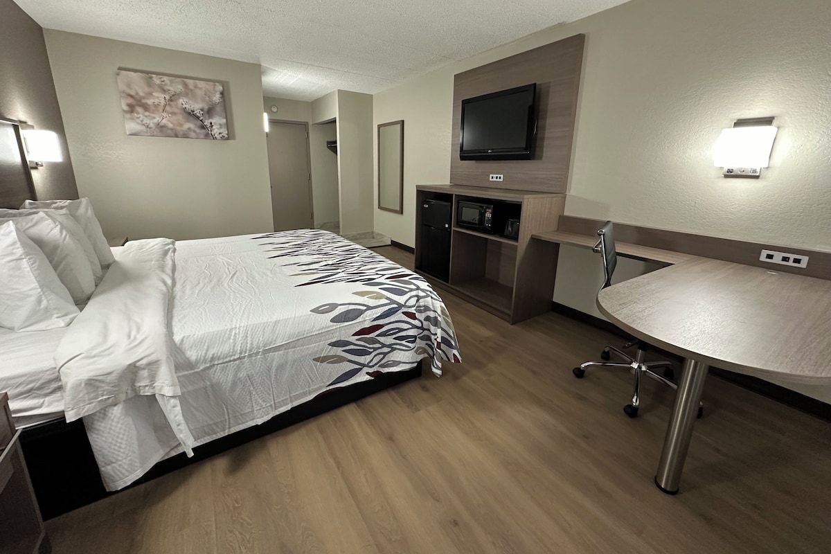A hotel room with a bed, a desk, a microwave, and a television.