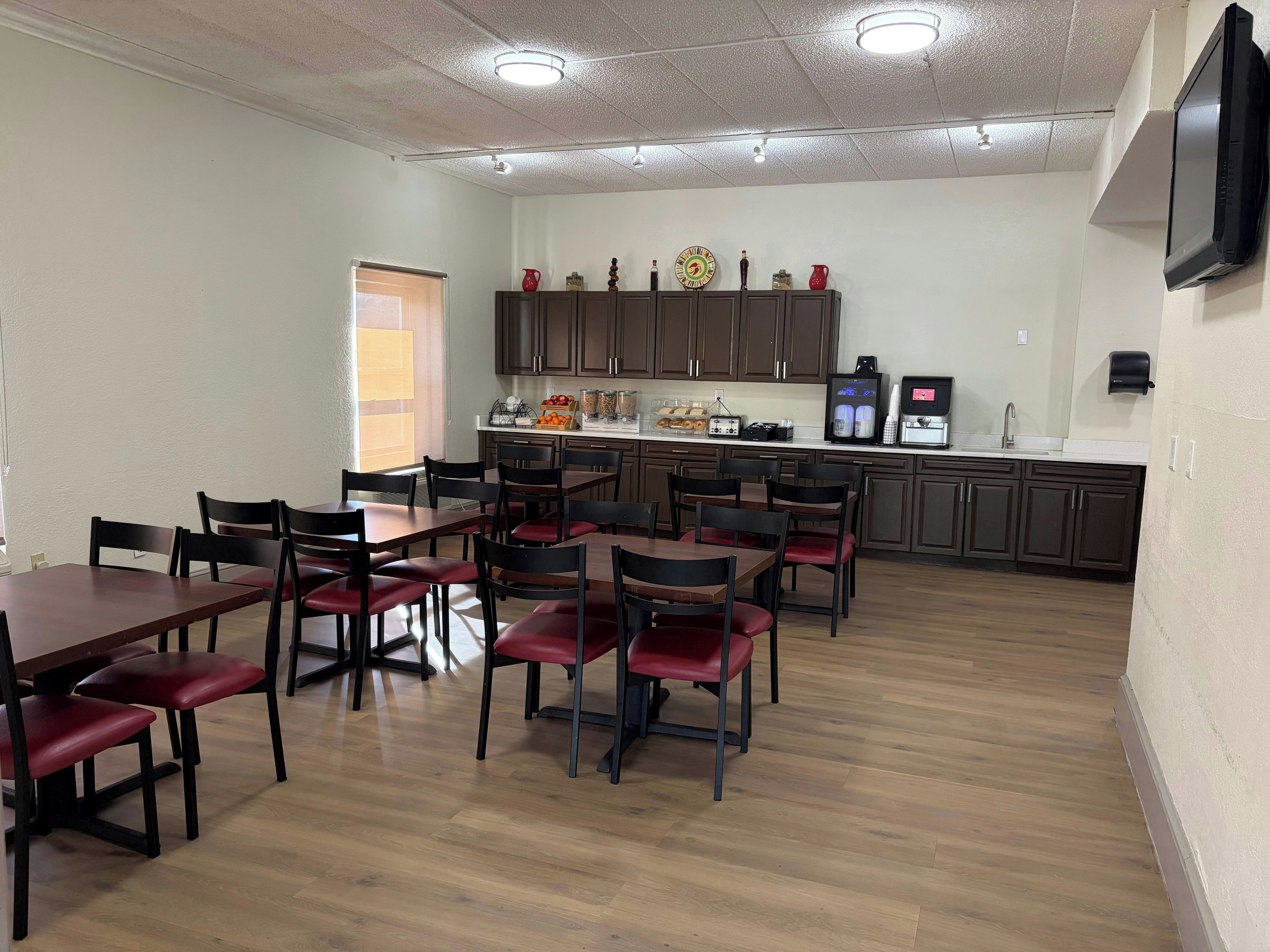 A dining area with wooden tables and chairs, a kitchen with appliances, and a television mounted on the wall.