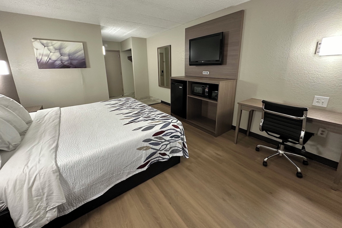 Ein Hotelzimmer mit einem Bett, einem Schreibtisch mit Stuhl, einem Fernseher und einer Mikrowelle.