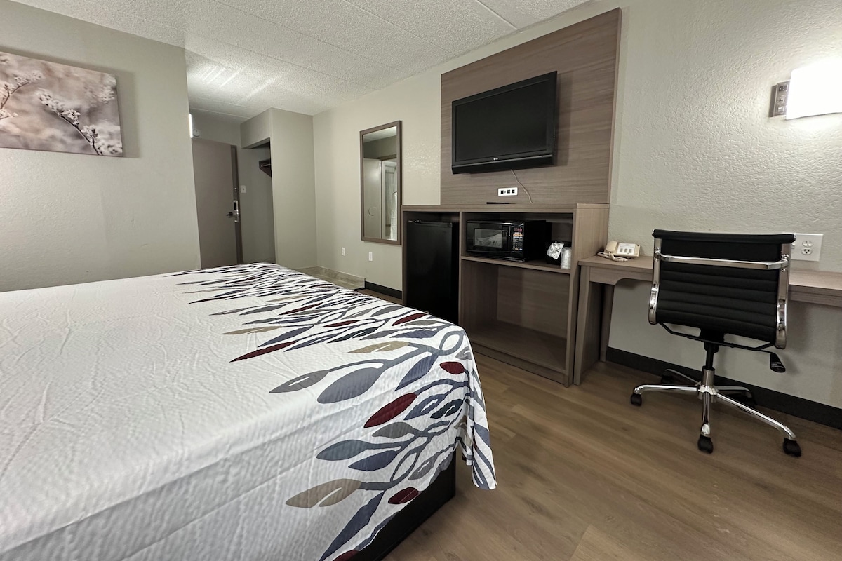 A hotel room with a bed, a desk with a chair, a television, a microwave, and a mirror.