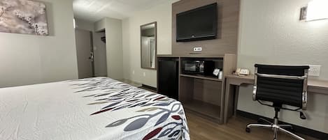 Ein Hotelzimmer mit Bett, Schreibtisch mit Stuhl, Fernseher, Mikrowelle und Spiegel.
