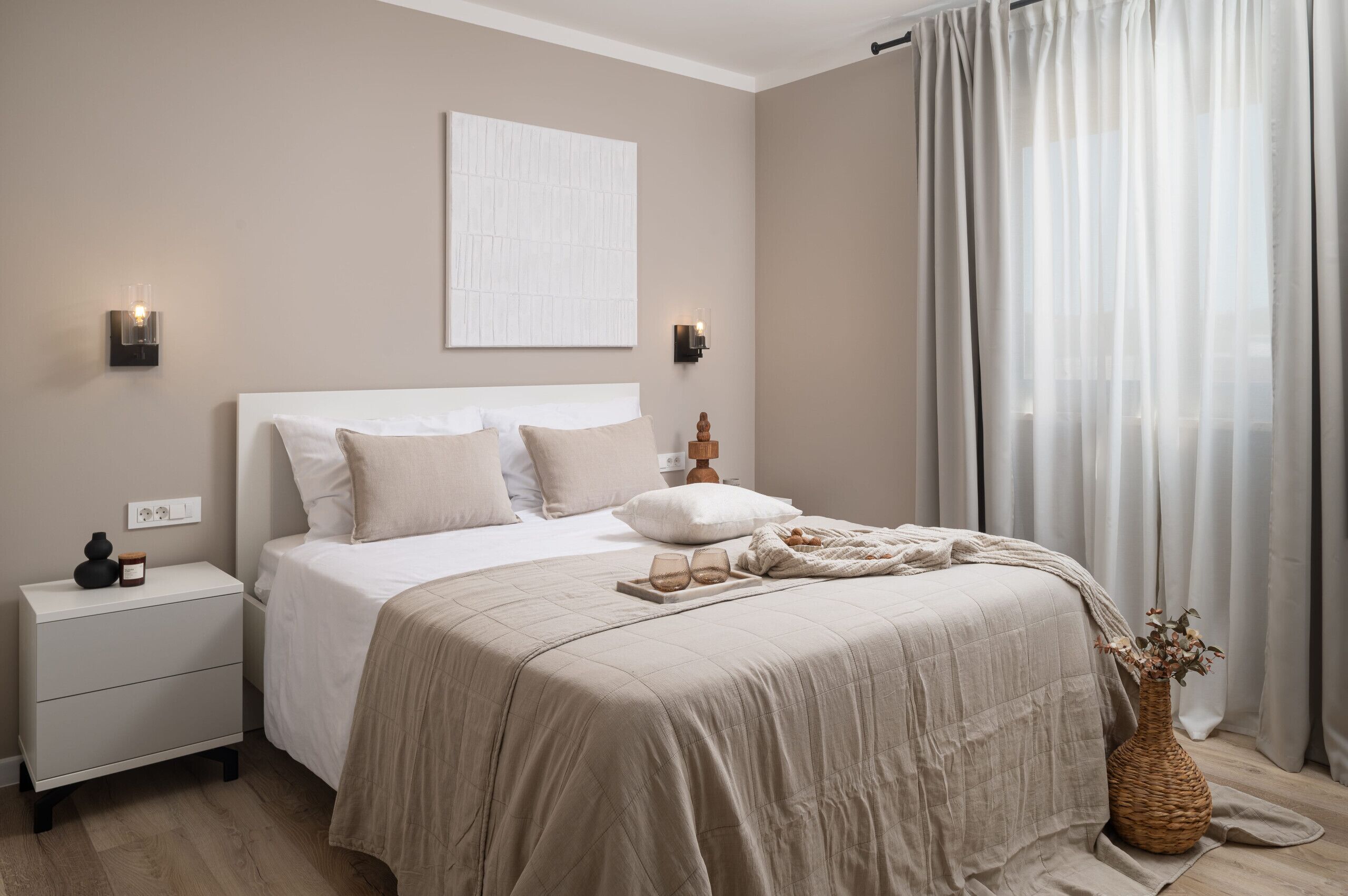A bedroom with a bed, nightstand, wall-mounted light, and a window with curtains.