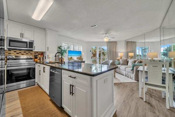 A modern kitchen with stainless steel appliances, a central island, and a view of the outdoors. - ⭐Steps to the Beach! Pool + Hot Tub-Complex Pool- Gulfview II 218⭐ (Miramar Beach)