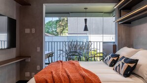 A modern hotel room with a large bed, a balcony with chairs, and a TV mounted on the wall.