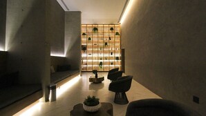 A modern lobby with a minimalist design, featuring a seating area with sofas and a coffee table, a wall-mounted plant display, and a clean, tiled floor.