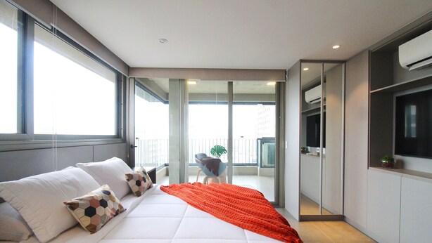 A modern hotel room with a large bed, a balcony with a chair, and a TV mounted on the wall.