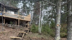 Eine Holztreppe führt zu einem Haus in bewaldeter Landschaft.