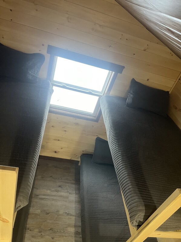Una habitación pequeña y acogedora con dos camas individuales, techo de madera y un tragaluz.