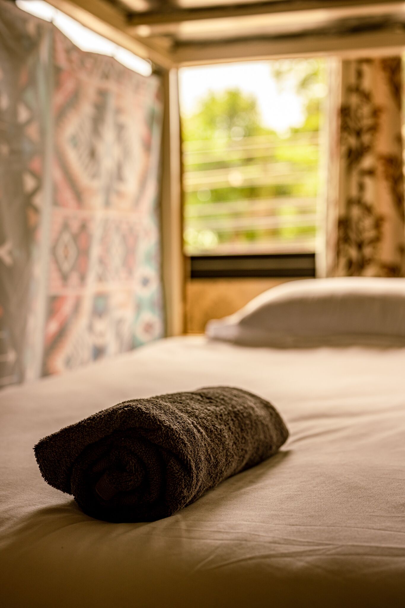 Una cama con una toalla enrollada, una ventana con persianas y una pared con diseño.