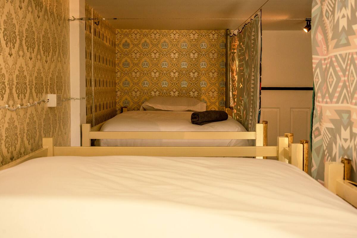 A bunk bed with a patterned wallpaper, a bedside table, and a curtain.