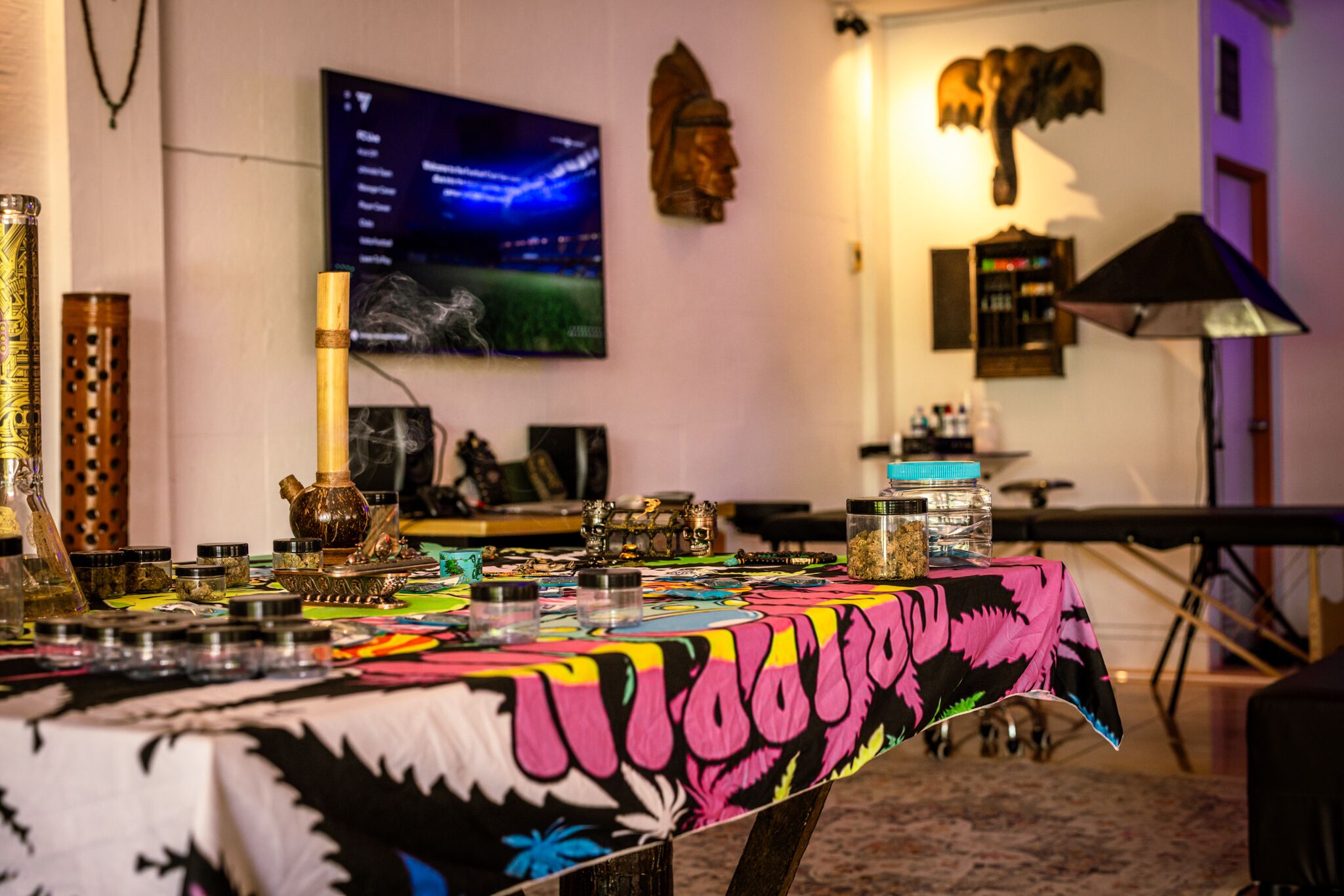A room with a table covered by a colorful tablecloth, various decorative items, a television, and wall art.