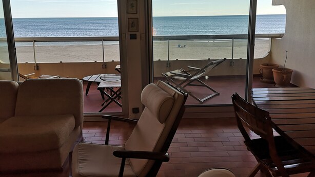 Un balcón con vista a la playa, una mesa, sillas y una planta en maceta.