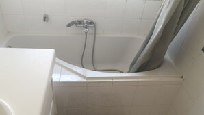 Un baño con bañera, ducha y suelo de baldosas.