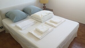 Una cama bien hecha con almohadas y toallas dobladas, una lámpara en una mesita de noche y un suelo de baldosas.