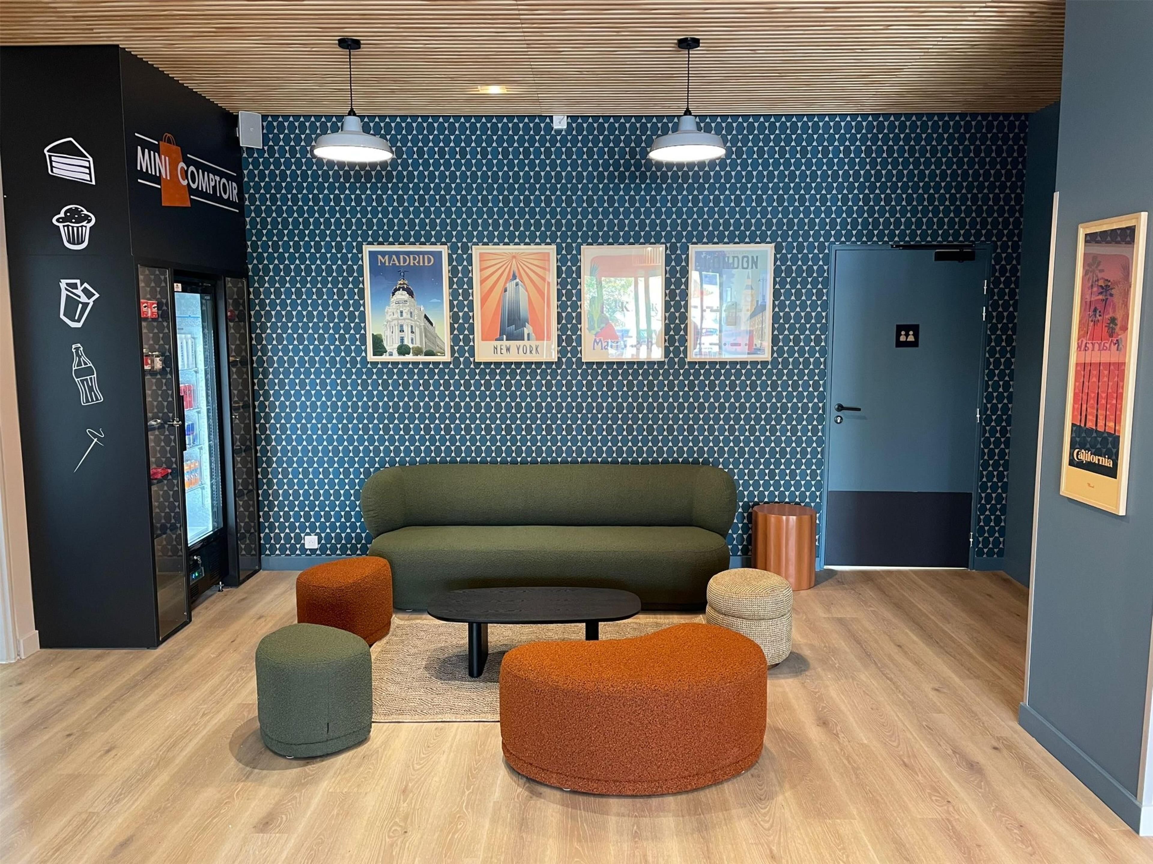 A modern lounge area with a blue patterned wall, a green sofa, and orange and green ottomans.