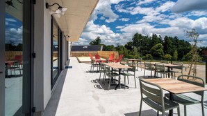 Un patio al aire libre con mesas y sillas, un paseo cubierto y vistas a árboles y un edificio al fondo.