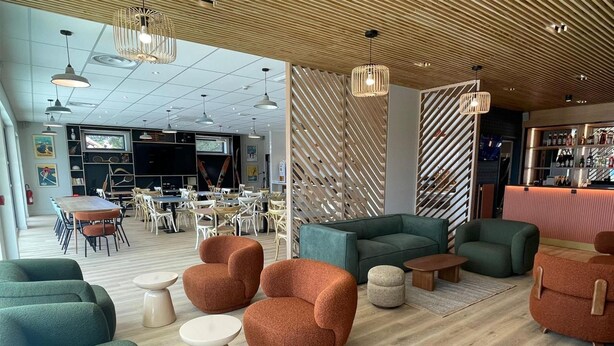 Un área de descanso moderna con asientos verdes y naranjas, un bar y un comedor con mesas y sillas.