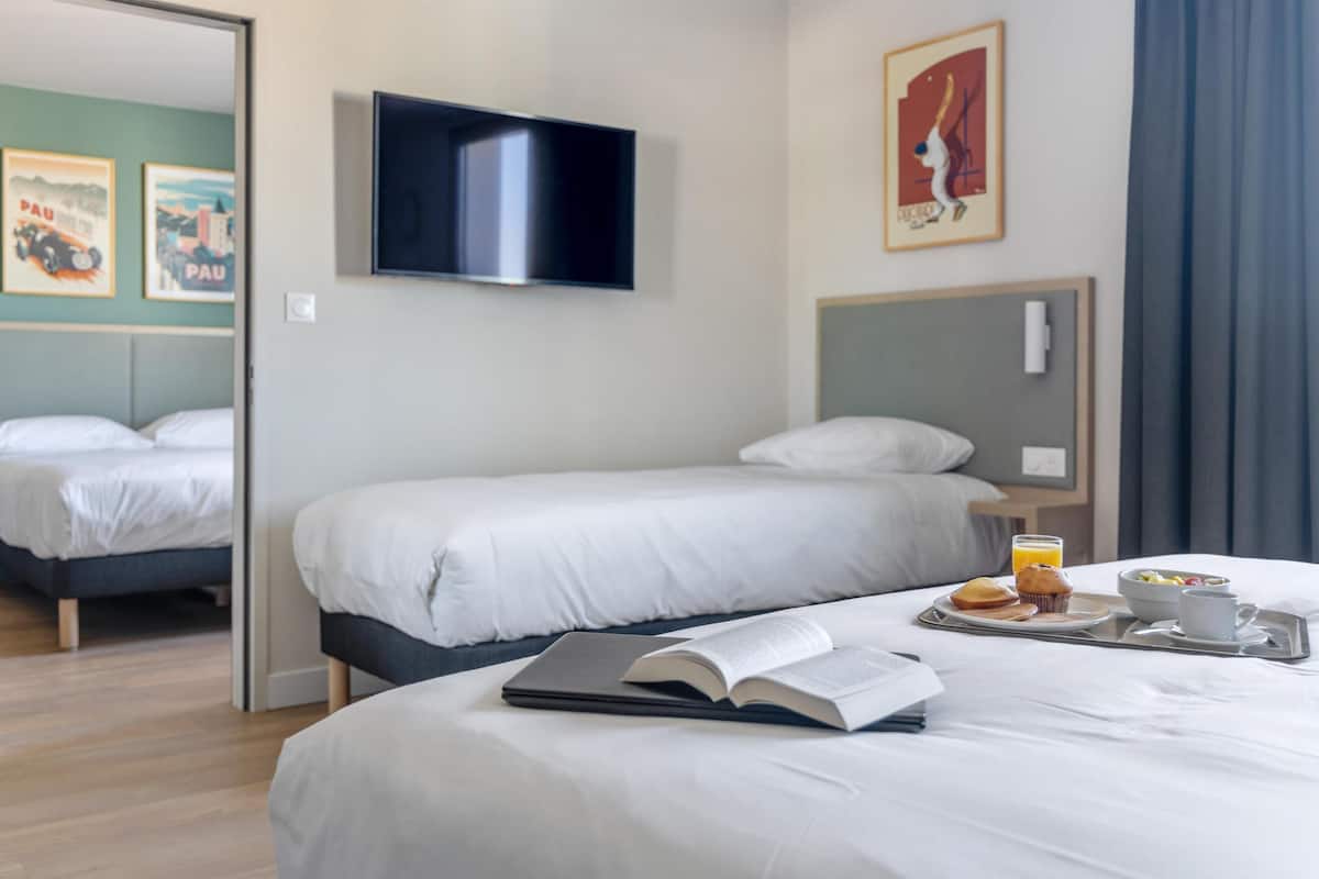 A hotel room with two beds, a flat-screen TV, artwork on the walls, and a breakfast tray on the bed.