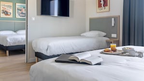 Habitación de hotel con dos camas, un televisor de pantalla plana, obras de arte en las paredes y una bandeja de desayuno en la cama.