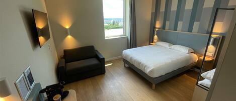 Una habitación de hotel moderna con una cama, un sofá, un escritorio con cafetera y una ventana con vistas.