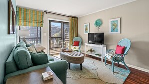 A living room with a sofa, ottoman, TV, and chairs. - Tilghman 146- 3BR Condo- Close to Main St (North Myrtle Beach)