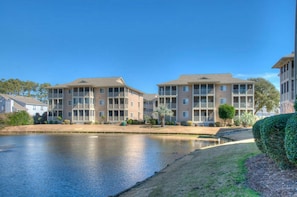 A multi-story residential building with a flat roof and large windows, situated next to a calm body of water.