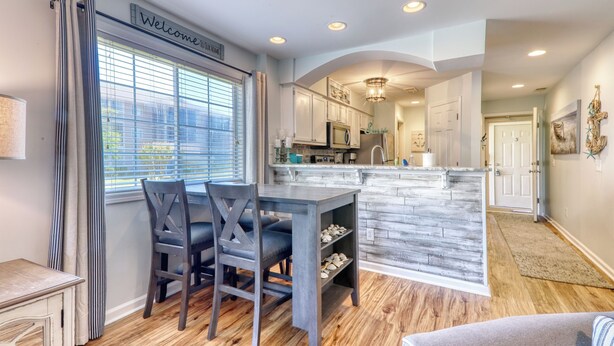 A modern kitchen with a central island, a dining area with a table and chairs, and a welcoming sign.