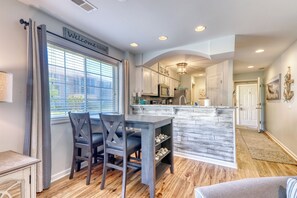A modern kitchen with a central island, a dining area with a table and chairs, and a welcoming sign.