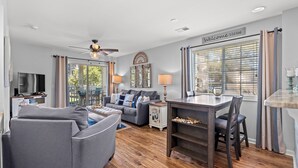 A modern living room with a grey sofa, a wooden dining table, and a ceiling fan.
