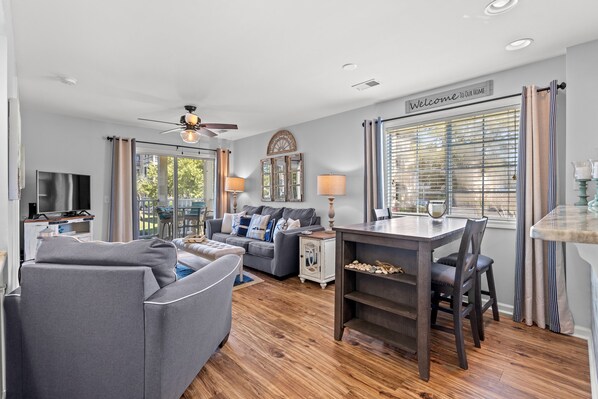A modern living room with a grey sofa, a wooden dining table, and a ceiling fan.