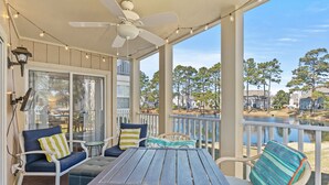 A covered outdoor seating area with a table and chairs, a ceiling fan, and a view of a lake and houses.
