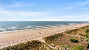 Una playa con cielo despejado, orilla de arena y algunas personas.
