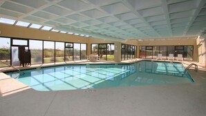 Una piscina interior con paredes de vidrio transparente, suelo de baldosas y techo con un diseño de cuadrícula.