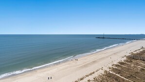 A wide beach with a wooden boardwalk, calm sea, and clear sky.