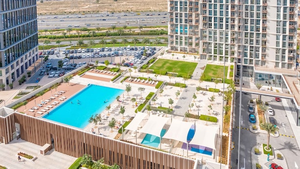 A high-rise building with a rooftop pool, landscaped areas, and a view of a busy road and distant buildings. - Luxury Brand New 2BR Apt at Dubai Hills (Dubai)