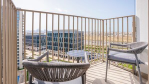 A balcony with two wicker chairs and a small table, overlooking a modern building complex and a cityscape. - Luxury Brand New 2BR Apt at Dubai Hills (Dubai)