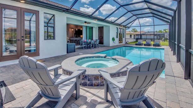 Ein überdachter Außenbereich mit Whirlpool, zwei Adirondack-Stühlen und einem Pool.