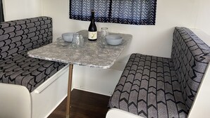 Una kitchenette compacta con una mesa, dos sillas, una botella de vino y una ventana con cortinas estampadas.