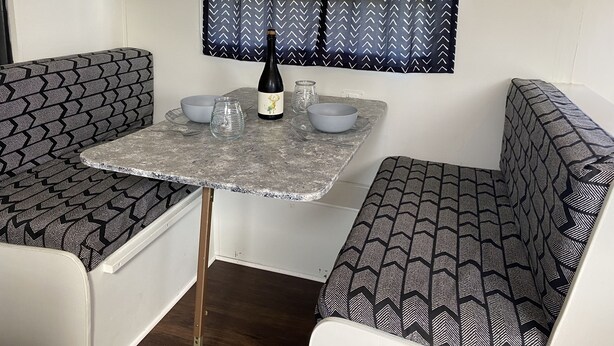 A compact kitchenette with a table, two chairs, a wine bottle, and a window with patterned curtains. - Wine Country Bell Tent w/ King Bed (Lodi)