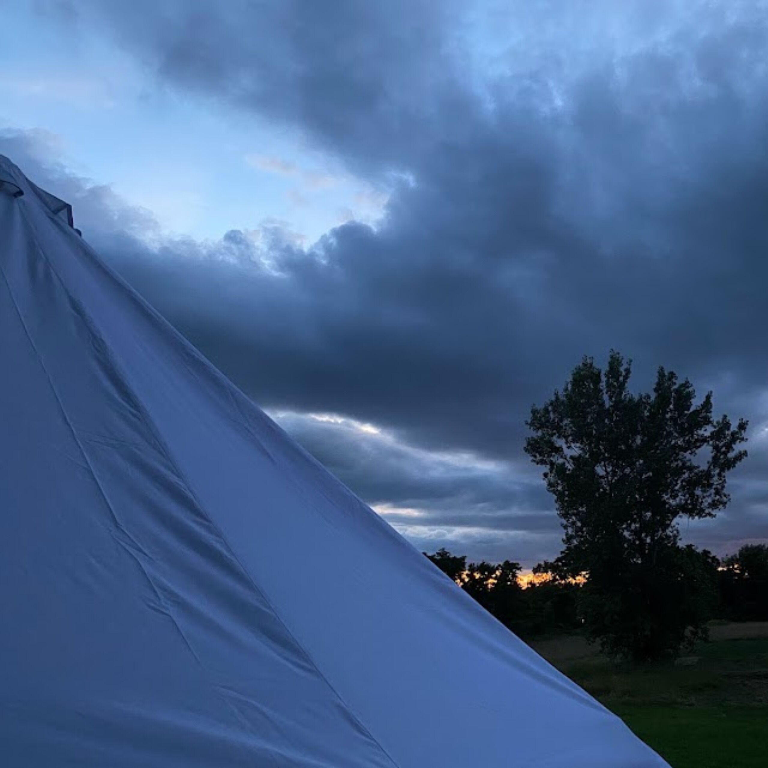 A tent set up outdoors with a cloudy sky in the background.