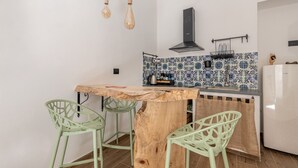 Μια κουζίνα με ένα ξύλινο πάγκο-νησίδα, δύο πράσινες καρέκλες, κρεμαστά φωτιστικά, έναν μαύρο απορροφητήρα και έναν τοίχο με πλακάκια.