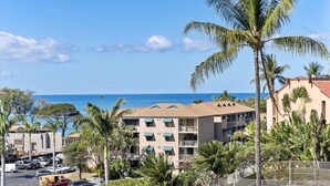 A beachfront hotel with multiple balconies, a parking area, and palm trees.