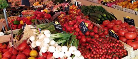 A market stall with various vegetables and fruits, including tomatoes, onions, and bell peppers.